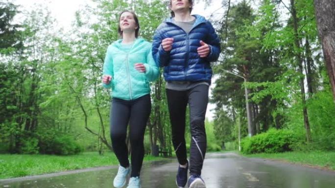 运动的年轻人跑步。夫妇在雨天在公园里跑步