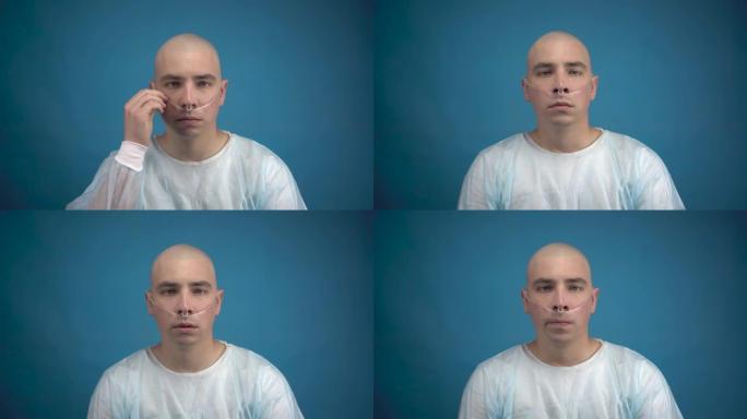一个秃头的年轻男子带着肿瘤悲伤地看着蓝色背景上的相机。病人拉直呼吸器的管子。化疗导致脱发。