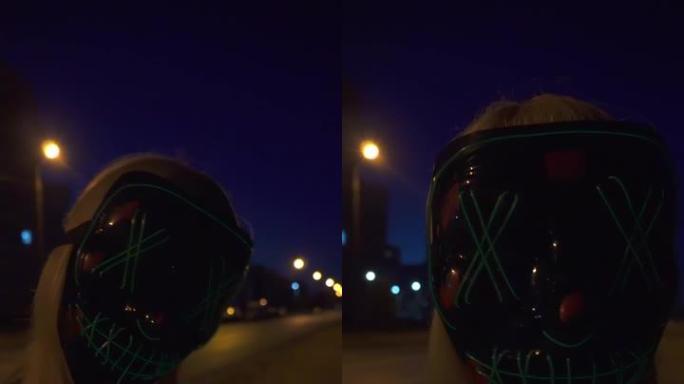 垂直视频。狂欢开始时，我突然出现。一个男人戴着异国情调的发光二极管面具。面具点亮，发光，街道，夜晚，