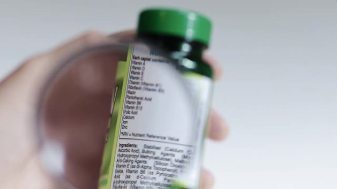 用放大镜检查一瓶补品上的营养信息标签的特写