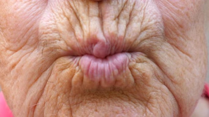 关闭成熟祖母的嘴唇。奶奶的嘴把空气吻送进镜头。皮肤皱纹的高级女性做接吻手势。慢动作