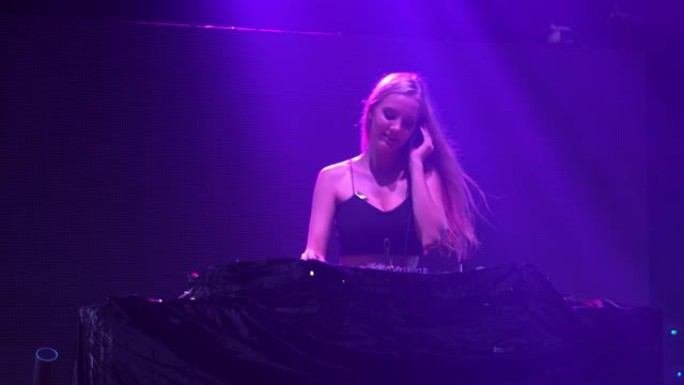 性感的女孩DJ在俱乐部的灯光和声音的音乐会上播放转盘电子舞曲和舞蹈。带有背景动画的抽象电子特效屏墙。