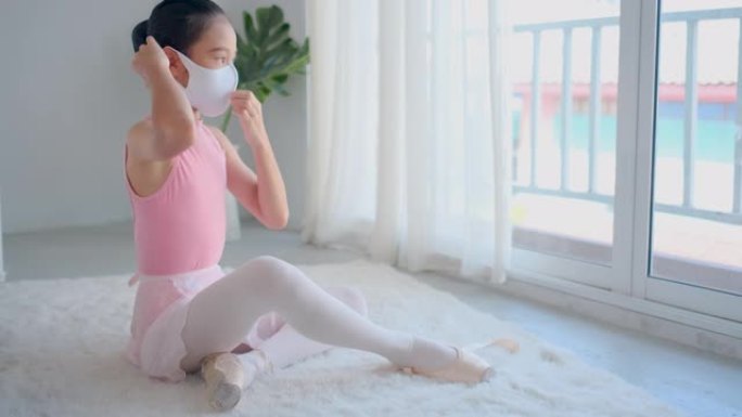 在covid病毒大流行期间，芭蕾小女孩在卧室里穿芭蕾舞鞋之前戴口罩，在她房子的玻璃窗前，她呆在家里和