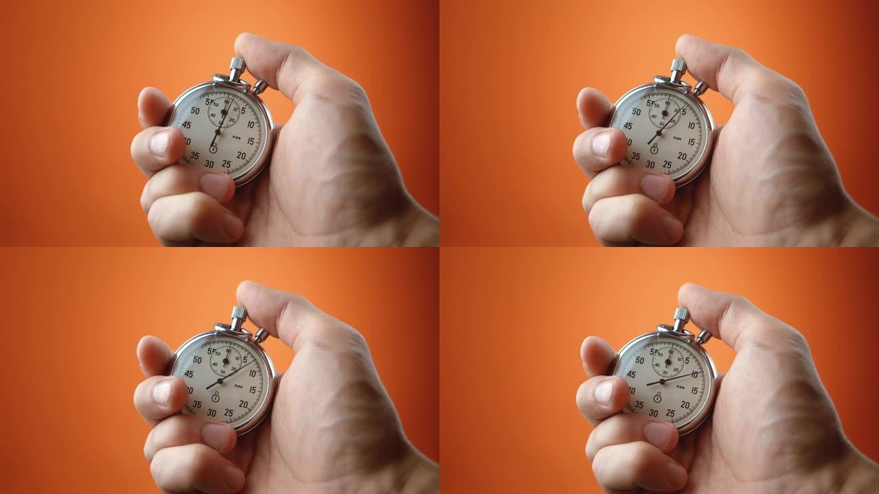 男性手持橙色背景的模拟秒表。时间开始与旧的计时器的人在运动概念中按开始按钮。时间管理理念。