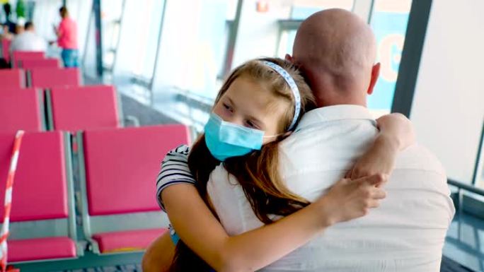 肖像，戴着防护面具的女童在机场候机室空座位的背景下拥抱她的父亲。冠状病毒疫情后航班开通