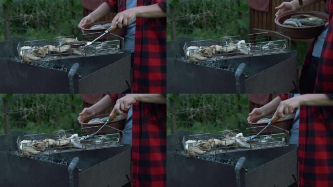 女人的手特写把煮熟的烤鱼放在盘子里。家庭在夏季小屋烧烤野餐。在烧烤架上准备了美味的鱼。