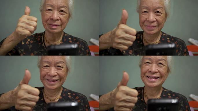 多莉万向节镜头: 快乐的亚洲高级女性在卧室里用手机示意再见，竖起大拇指，爱。聊天和观看视频。概念: 