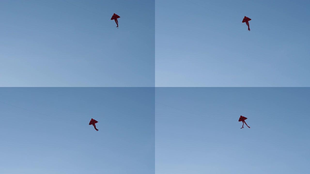 一只红色的风筝在蓝色的夏日天空的背景下在空中飞翔。