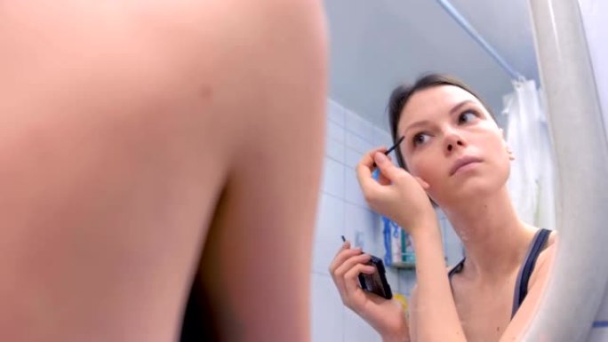 美丽的黑发女人在镜子前画浴室的眉毛。
