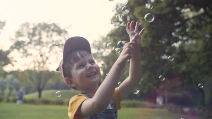 小男孩在夏季公园抓肥皂泡
