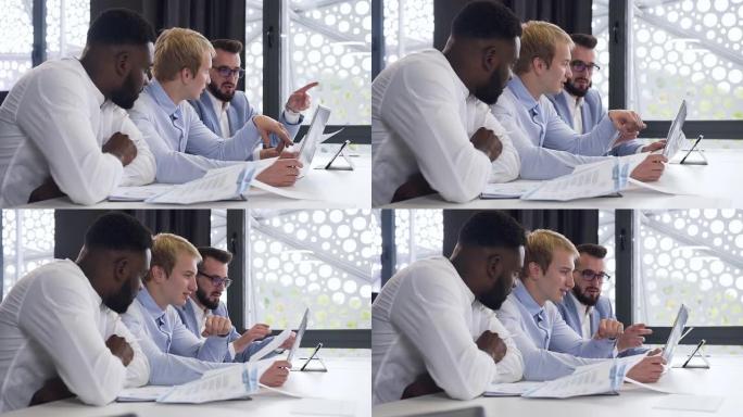 英俊的多种族30年代经理看着电脑屏幕，在办公室讨论他们的商业计划