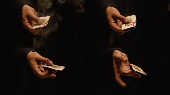 魔术师手表演纸牌把戏的特写。黑色背景上有烟的燃烧卡片。卡片机械师手里拿着旋转火焰卡片。慢动作在ARR