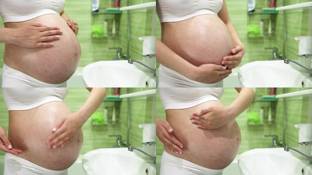 怀孕的女孩在浴室用奶油润滑胃以防止妊娠纹