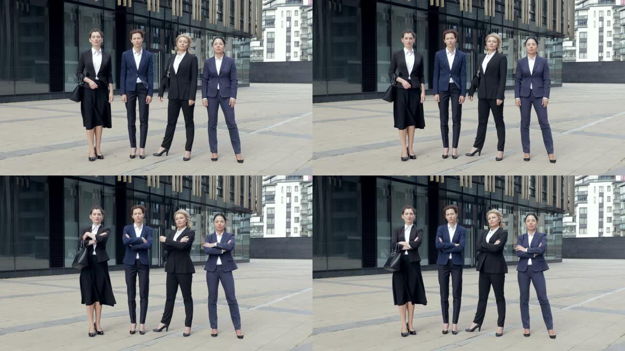 严肃的公司员工站在办公室旁边双手交叉。一群成功的女员工穿着西装微笑着看着镜头。团队肖像概念