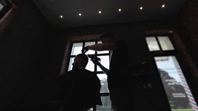 理发师在男性沙龙用电动修剪器做发型。黑发理发师戴着黑色手套在理发店为客户理发。带修剪器和发刷的造型师