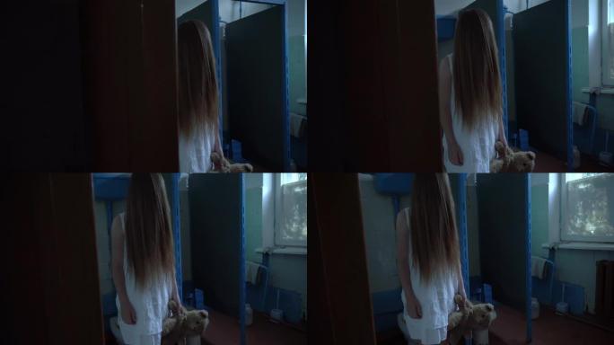 在旧学校里，在厕所里的一个房间里，一个女孩穿着白色连衣裙，脸上留着长发。在他的手中，他有一只泰迪熊，