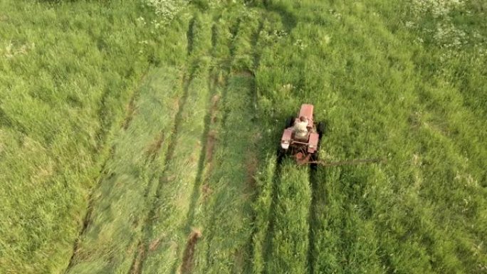 没有出租车的老式拖拉机上的农民用割草机割草穿过草地