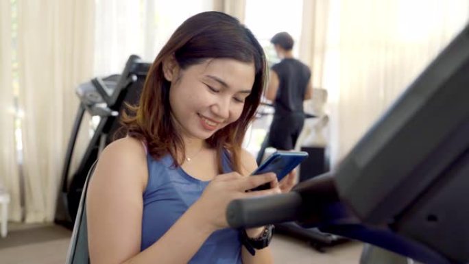 使用手机的年轻亚洲女性在健身馆向社交媒体拍照和发短信。
