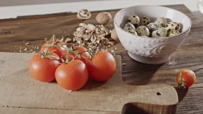 沙拉烹饪的天然成分背景-陶瓷碗中的鹌鹑蛋，湿西红柿，木板上的核桃，厨房桌子。多莉-在4k慢动作。