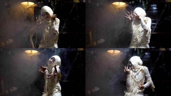 穿着万圣节木乃伊服装的女孩在古老的黑暗哥特式室内摆出姿势并吓scar的电影镜头，上面覆盖着蜘蛛网和雾