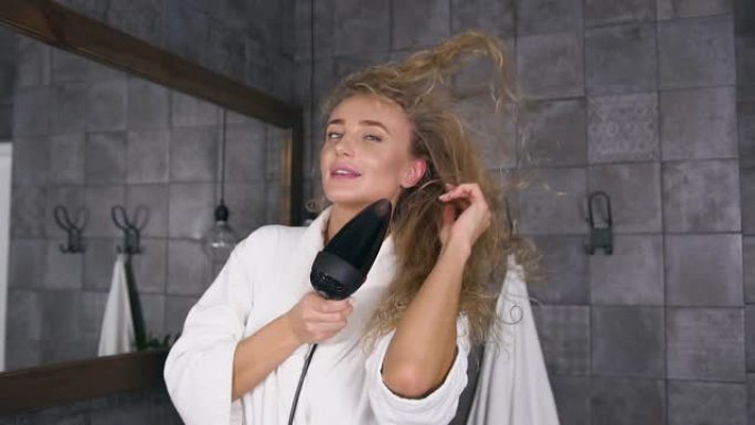 美丽的金发碧眼的女人在浴室里用吹风机吹干头发的前视图