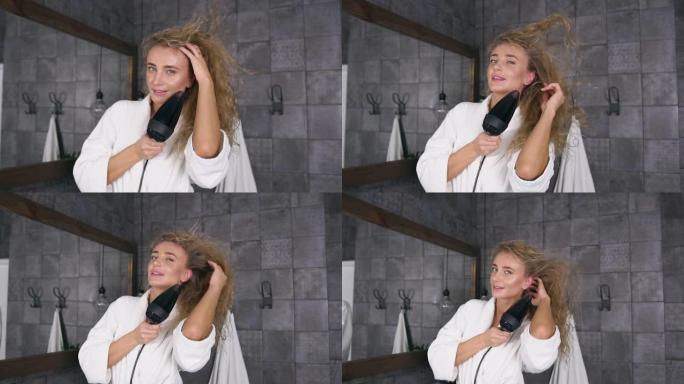 美丽的金发碧眼的女人在浴室里用吹风机吹干头发的前视图