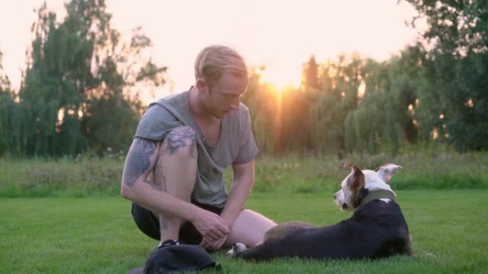 男子坐在草地上与狗玩耍