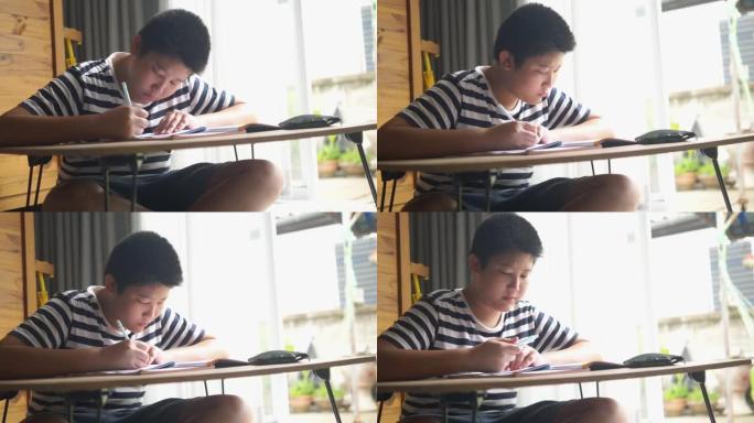 亚洲青春期男孩坐在地板上，在家窗户附近做作业，生活方式概念。