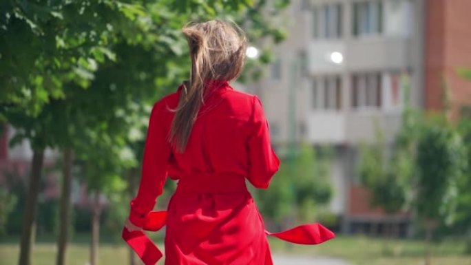 女人在户外散步的慢动作。城市中一位穿着红色连衣裙的年轻女性的后景。迷人女孩的长发。