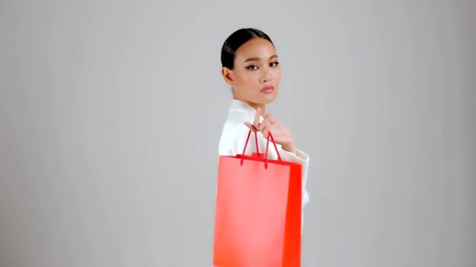 美丽的亚洲现代外观女商人拿着红色购物袋，看着相机