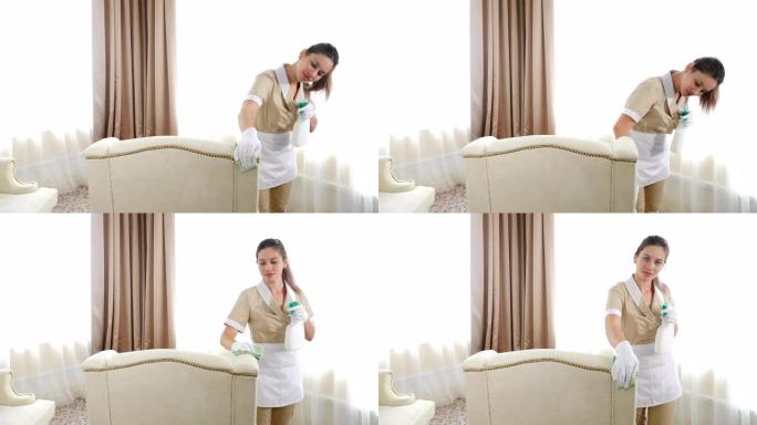 酒店清洁。柔软的家具表面由漂亮的女仆用手擦拭干净。女人用蘸有洗涤剂的擦拭布去除软垫家具上的脏污渍。在