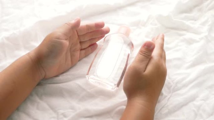 小手在白色织物背景上拿着透明塑料瓶油的特写镜头。关心柔软的身体婴儿皮肤。