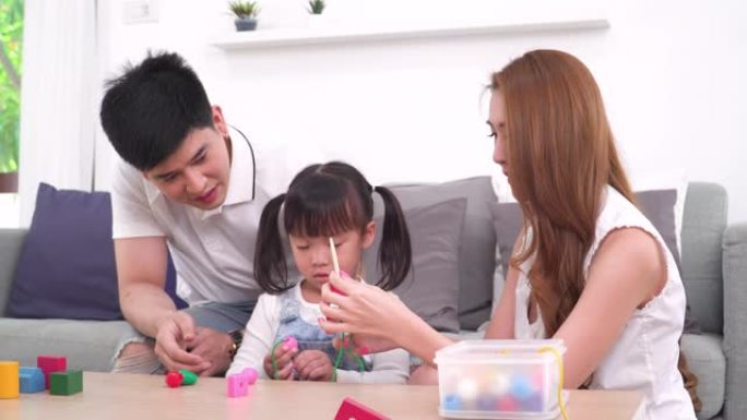 一个亚洲儿童和一个孩子在学龄前的家庭的生活概念。亚洲可爱的女孩坐在地板上，玩耍，在周末与年轻的父亲和