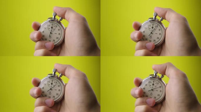 黄色背景上的男性手握模拟秒表。时间开始与旧的计时器的人在运动概念中按开始按钮。时间管理理念。