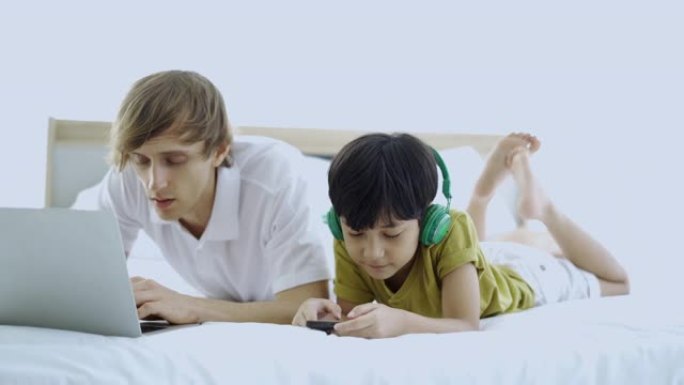 父子俩躺在床上的笔记本电脑上看动画片。