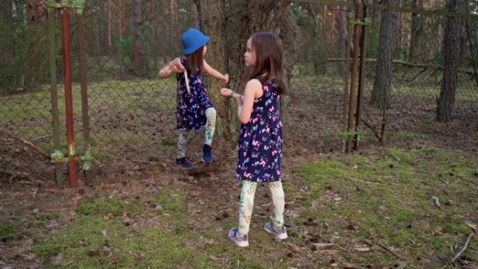 穿着连衣裙的女孩穿过夏季森林中篱笆的一个洞