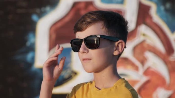 戴着墨镜的快乐男孩在阳光明媚的夏日慢动作中站在明亮的城墙的背景上微笑。暑期学校假期。旅游。生活方式
