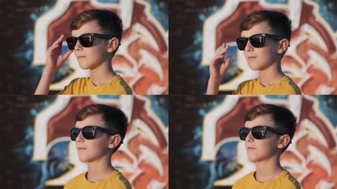 戴着墨镜的快乐男孩在阳光明媚的夏日慢动作中站在明亮的城墙的背景上微笑。暑期学校假期。旅游。生活方式