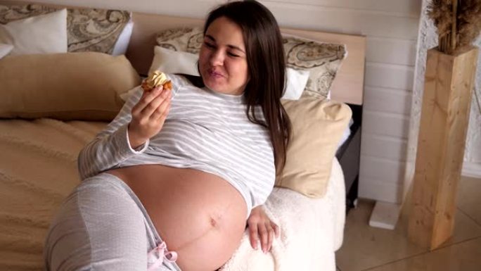 快乐的孕妇躺在床上吃甜蛋糕。