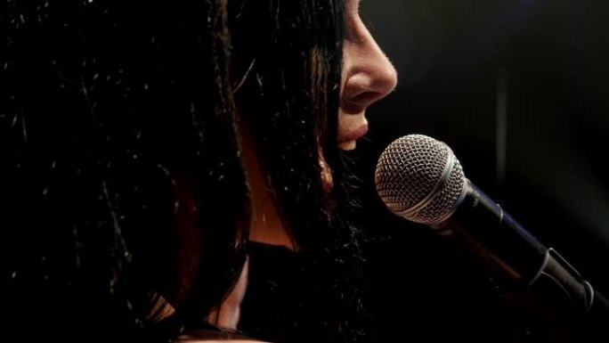 年轻女子在空荡荡的舞台上用麦克风唱一首悲伤的歌，特写。
