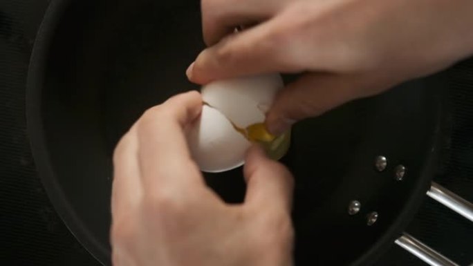双手在黑锅上打碎鸡蛋的慢动作镜头