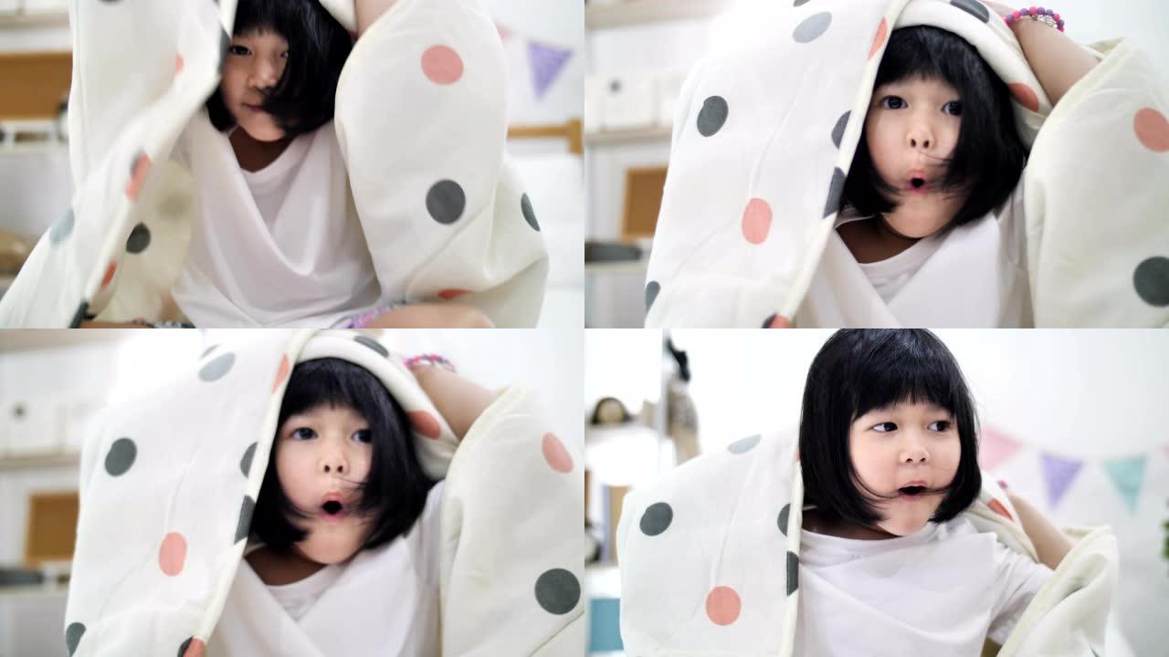 可爱的亚洲小女孩的慢动作用毯子盖住。玩捉迷藏，偷看嘘声