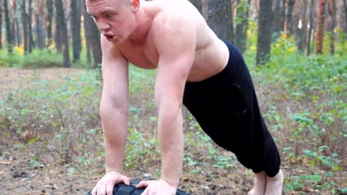 强壮的人在森林里做俯卧撑。男性运动员在大自然中锻炼。年轻人在户外训练。肌肉发达的运动员表现出艰苦而激