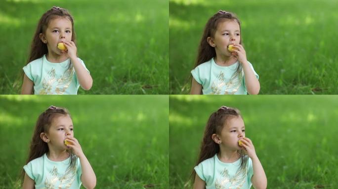 绿色草坪上的一个小女孩咬掉了成熟的杏子。肖像。