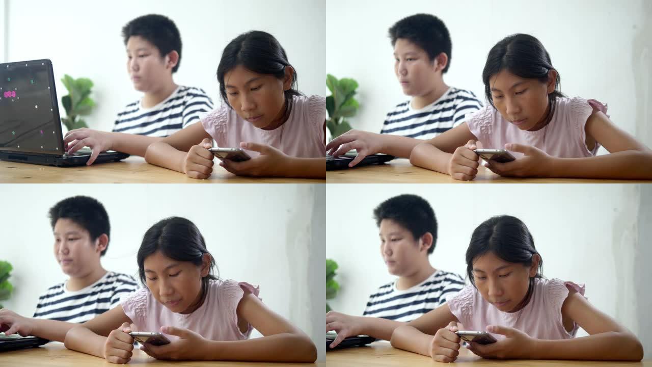快乐的亚洲男孩和女孩在家里通过笔记本电脑和智能手机一起玩网络游戏，生活方式概念。