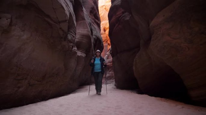 女人在带有红色橙色岩石的深槽峡谷的干燥河床上徒步旅行