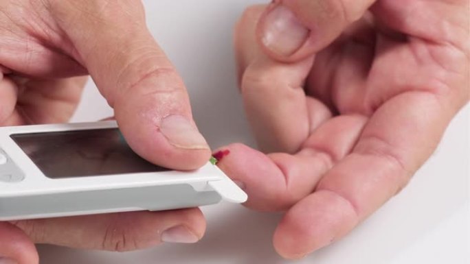 从手指取血到测定血糖的试纸的过程，一个人的手拿着带有监视器的电子血糖仪，血液从手指流出