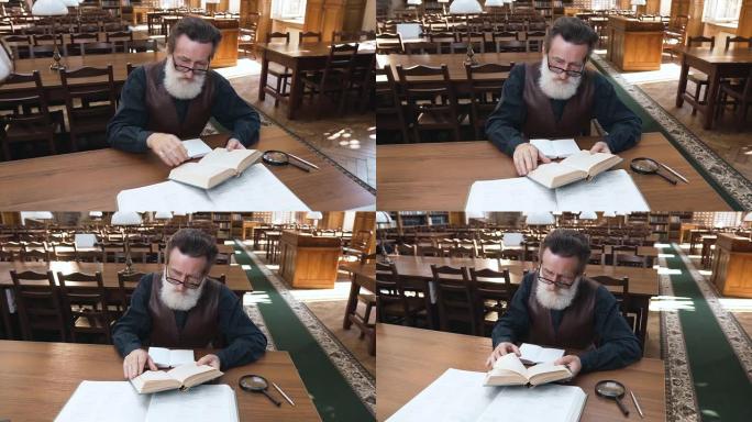 有吸引力的人专注于阅读大胡子的老人眼镜坐在图书馆的桌子旁看书