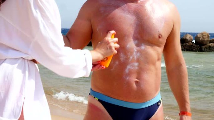 特写，在男人皮肤上涂抹防晒霜或喷雾乳液。在海滩上，在烈日下，在大海的背景下。防晒和防紫外线。皮肤保护