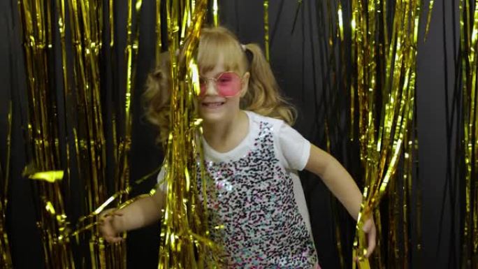 快乐的孩子在闪亮的箔流苏金色窗帘中跳舞，玩耍，鬼混。金发小女孩